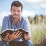 man reading book in grass field