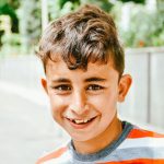 boy in orange and gray crew neck shirt smiling