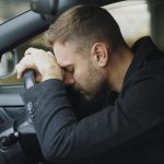 Man resting head on steering wheel in car.